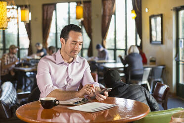 Hispanic businessman using cell phone in coffee shop - BLEF08246