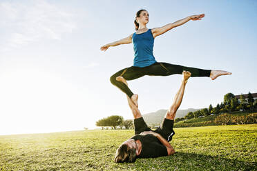 Couple stretching while doing acroyoga in public park stock photo