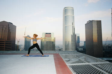 Gemischtrassige Frau übt Yoga auf einem städtischen Hausdach - BLEF08275