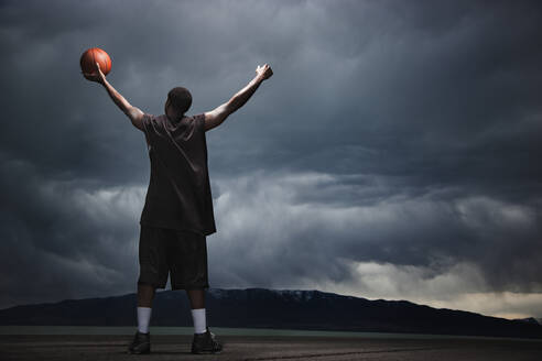 Gemischtrassiger Basketballspieler mit Gewitterwolken in der Ferne - BLEF08327