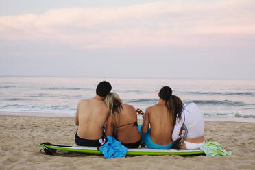 Teenage couples sitting on surfboard on beach - BLEF08381