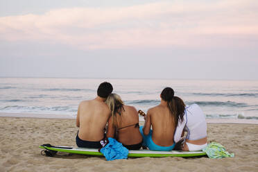 Teenager-Pärchen sitzt auf einem Surfbrett am Strand - BLEF08381