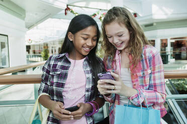 Freunde schauen in einem Einkaufszentrum auf ihr Handy - BLEF08488