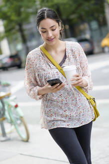 Hispanic woman using cell phone on city sidewalk - BLEF08530