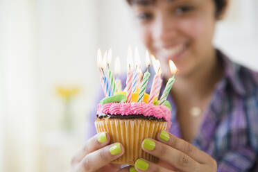 Gemischtrassige Frau hält Muffin mit Geburtstagskerzen - BLEF08544