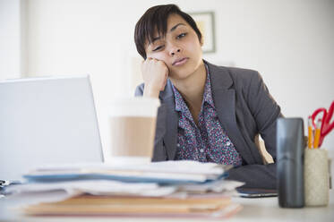 Bored mixed race businesswoman sitting at office desk - BLEF08553