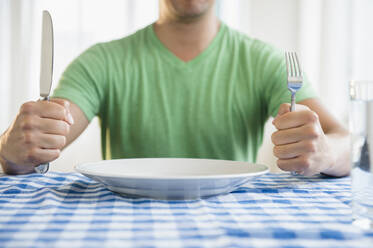 Mixed race man holding fork and knife at table - BLEF08556