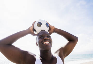 Mixed race man holding soccer ball on beach - BLEF08584