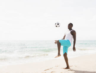 Gemischtrassiger Mann spielt mit Fußball am Strand - BLEF08586