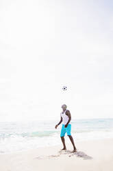 Gemischtrassiger Mann spielt mit Fußball am Strand - BLEF08587