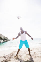 Gemischtrassiger Mann spielt mit Fußball am Strand - BLEF08588