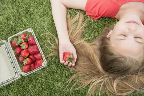 Kaukasisches Mädchen hält Erdbeeren auf grasbewachsenem Rasen, lizenzfreies Stockfoto