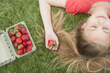 Caucasian girl holding strawberries on grassy lawn - BLEF08627