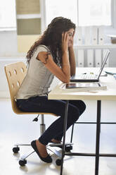 Frustrierte gemischtrassige Geschäftsfrau, die an einem Laptop am Schreibtisch im Büro arbeitet - BLEF08657