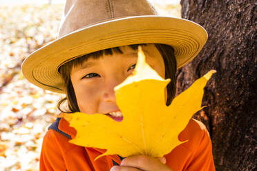 Nahaufnahme eines lächelnden gemischtrassigen Jungen, der ein Herbstblatt hält - BLEF08694