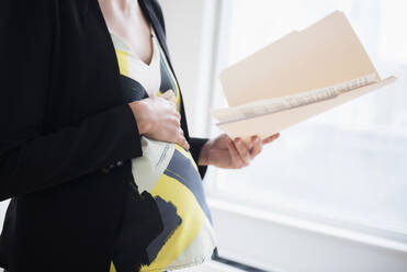 Pregnant Caucasian businesswoman holding files in office - BLEF08703