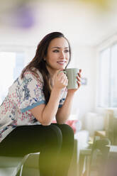 Woman drinking cup of coffee in living room - BLEF08706