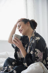 Woman drinking cup of coffee on bed - BLEF08714