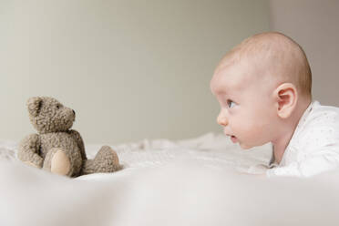 Kaukasisches Baby starrt auf Teddybär auf Bett - BLEF08721