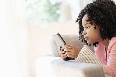 Afroamerikanisches Mädchen benutzt Mobiltelefon auf dem Sofa - BLEF08735