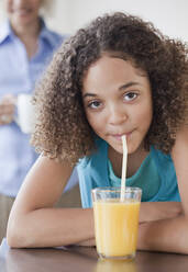 Gemischtrassiges Mädchen trinkt Orangensaft mit Strohhalm - BLEF08752