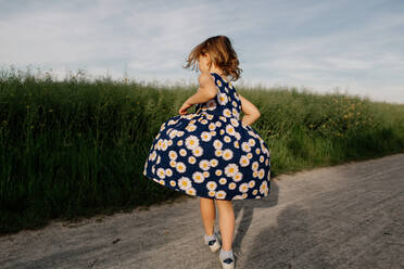 Rückenansicht eines kleinen Mädchens im Sommerkleid mit Blumenmuster, das auf einem Feldweg tanzt - OGF00010