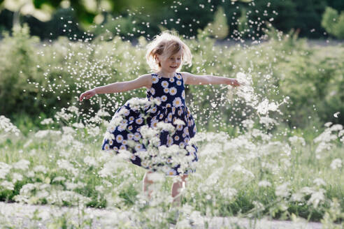 Porträt eines lächelnden kleinen Mädchens, das mit Pusteblumensamen spielt - OGF00013