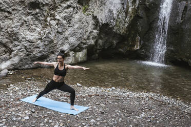 Woman practising yoga at waterfall, warrior pose - LJF00367