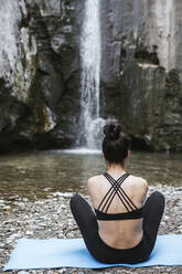 Rückansicht einer Frau, die am Wasserfall Yoga übt - LJF00369