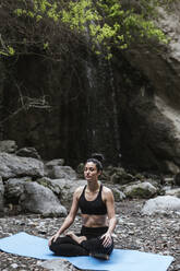 Frau übt Yoga und meditiert am Wasserfall - LJF00371