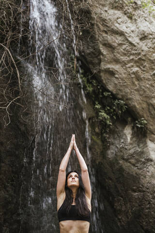 Frau übt Yoga am Wasserfall, Baumstellung, lizenzfreies Stockfoto