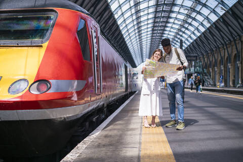 Junges Paar steht auf einem Bahnsteig und betrachtet eine Karte, London, UK, lizenzfreies Stockfoto