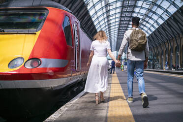 Rückenansicht eines jungen Paares, das Hand in Hand auf dem Bahnsteig geht, London, UK - FBAF00863