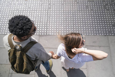 Junges Paar steht Hand in Hand am Straßenrand und schaut nach rechts - FBAF00868