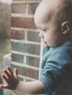 Kleines Mädchen blickt durch ein mit Regentropfen bedecktes Fenster - IHF00167
