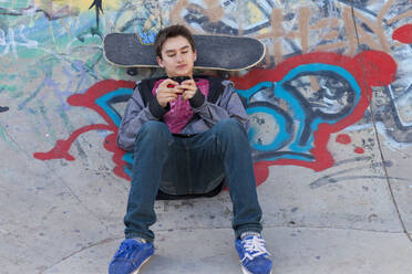 Gemischte Rasse Junge mit Skateboard Textnachrichten auf Handy - BLEF08806