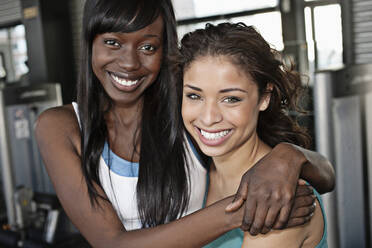 Lächelnde Frauen umarmen sich im Fitnessstudio - BLEF08829
