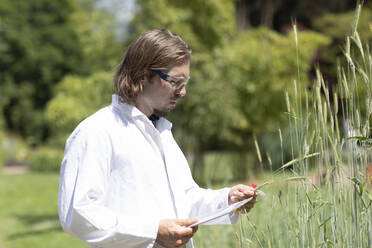 Researcher in a laboratory coat examining plants outside - SGF02395