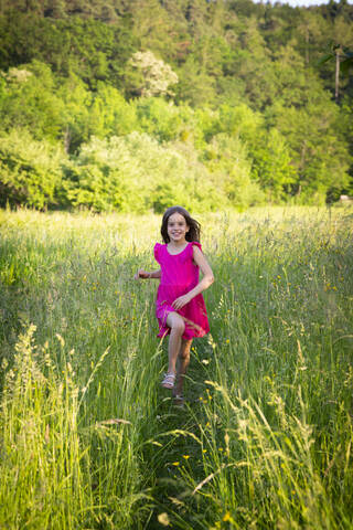 Porträt eines kleinen Mädchens, das lächelnd über eine ländliche Wiese auf die Kamera zuläuft, lizenzfreies Stockfoto