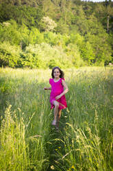 Porträt eines kleinen Mädchens, das lächelnd über eine ländliche Wiese auf die Kamera zuläuft - LVF08133
