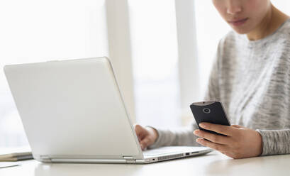 Hispanic woman using cell phone and laptop - BLEF08860