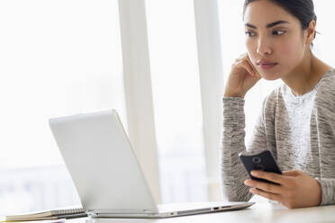 Hispanic woman using cell phone and laptop - BLEF08861