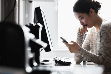 Hispanische Frau, die ein Mobiltelefon am Computer benutzt - BLEF08865