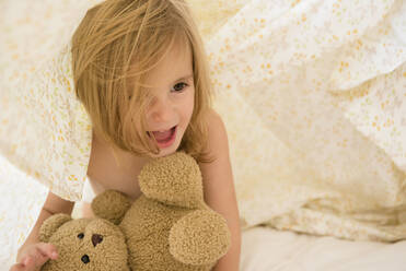 Caucasian girl playing with teddy bear under blankets - BLEF08907