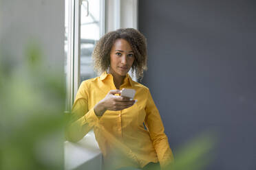 Porträt einer jungen Frau mit gelbem Hemd, die ein Mobiltelefon benutzt - MOEF02324