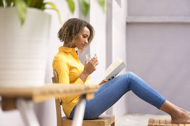 Young woman relaxing with glass of water reading a book - MOEF02328