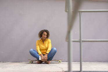 Porträt einer jungen Frau Buch sitzend barfuß auf Skateboard - MOEF02329