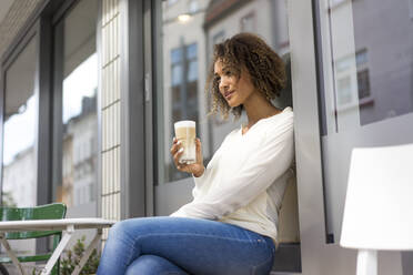 Junge Frau entspannt sich in einem Straßencafé mit Latte Macchiato - MOEF02348