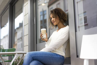 Young woman relaxing at pavement cafe with Latte Macchiato - MOEF02348