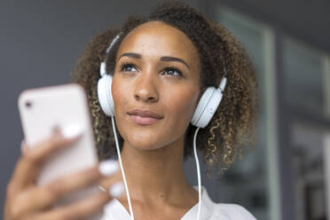 Porträt einer jungen Frau mit Smartphone und weißen Kopfhörern - MOEF02356